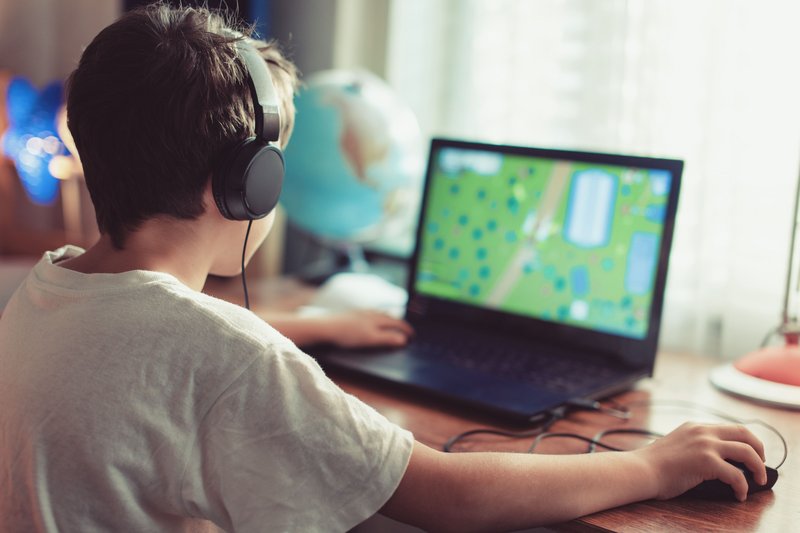 Kind sitzt vor dem Laptop und spielt ein Spiel.