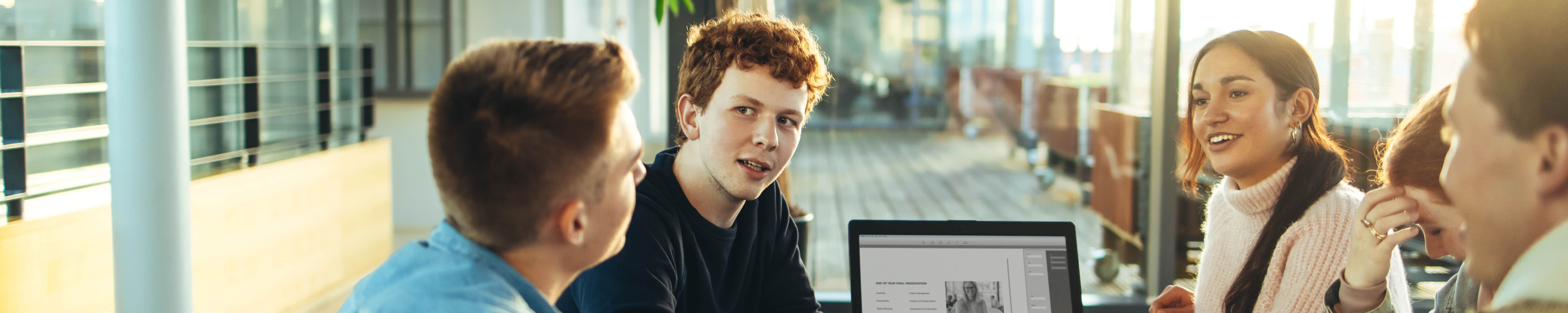 Jugendliche diskutieren an rundem Tisch, Laptop mit Pitch in der Tischmitte