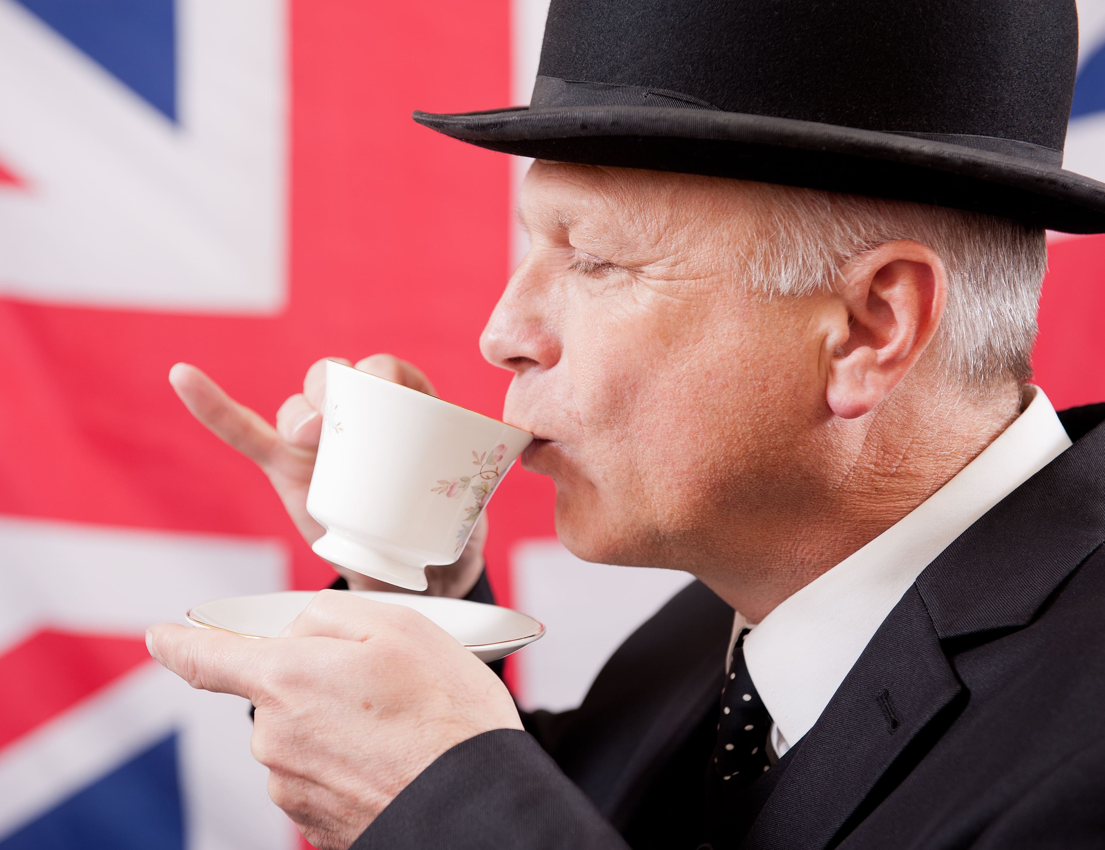 Mann mit Zylinder trinkt Tee vor einer britischen Flagge