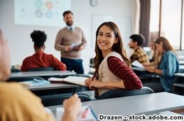 Frau sitzt in einem Klassenraum und schaut freundlich nach hinten