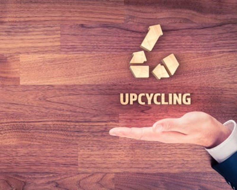 Der Schriftzug Upcycling auf einer Hand vor einem Holz-Hintergrund