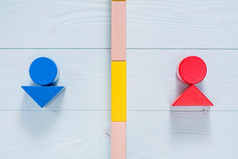 Ein blaues Dreieck und Kreis auf der einen Seite einer Bauklotzmauer und ein Kreis und ein Dreieck in rot auf der anderen Seite. 