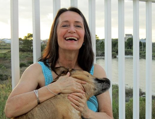 Frau lachend mit einem Hund auf und einem hohen weißen Geländer hinter sich