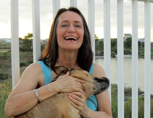 Frau lachend mit einem Hund auf und einem hohen weißen Geländer hinter sich