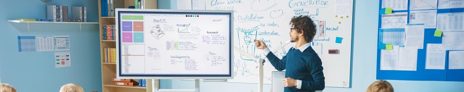 Dossier Unterrichten mit Whiteboards Lehrer steht an einem interaktiven Whiteboard vor der Klasse