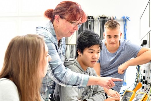 Eine Lehrerin erklärt älteren Schülern etwas an elektronischen Geräten 