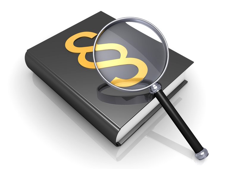 Eine Lupe auf einem Buch auf dem ein Paragraph gedruckt ist. 