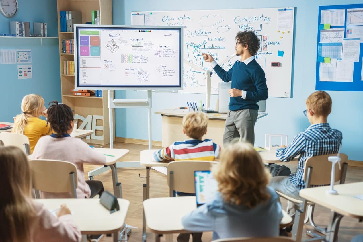 Lehrer steht an einem interaktiven Whiteboard vor der Klasse