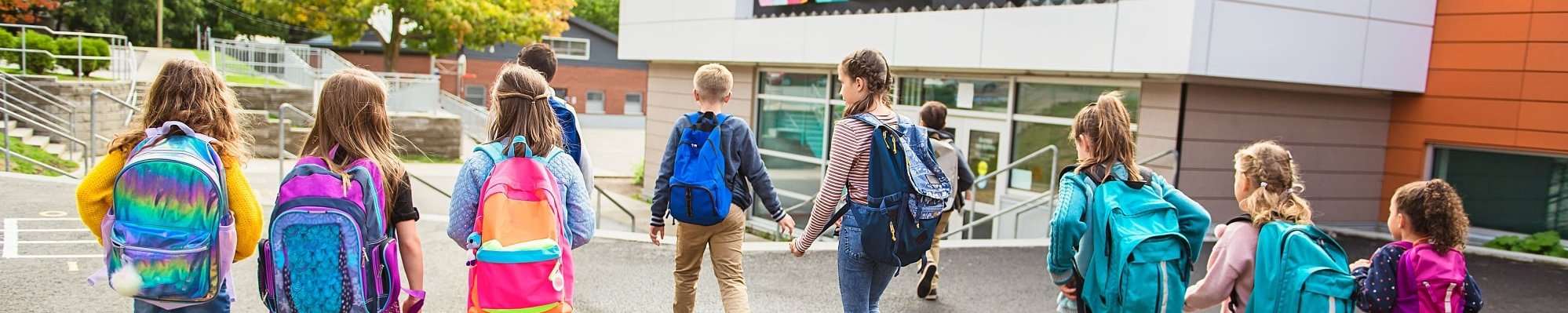 Schülerinnen und Schüler laufen auf ein Schulhaus zu 