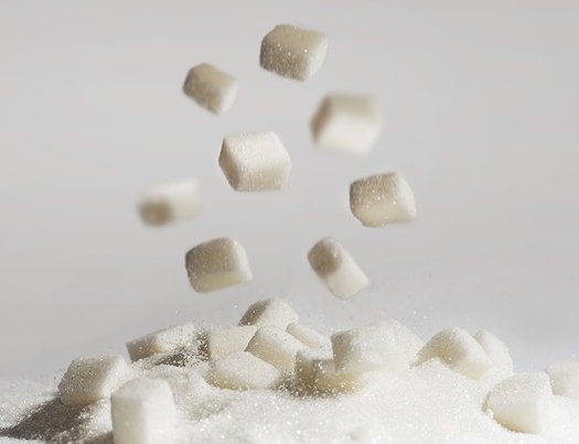 Zuckerwürfel fallen in einen Berg aus kleinen Teilchen von Zucker