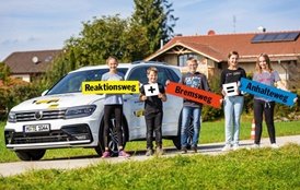 Kinder mit Schildern vor einem SUV (Reaktionsweg + Bremsweg = Anhalteweg)