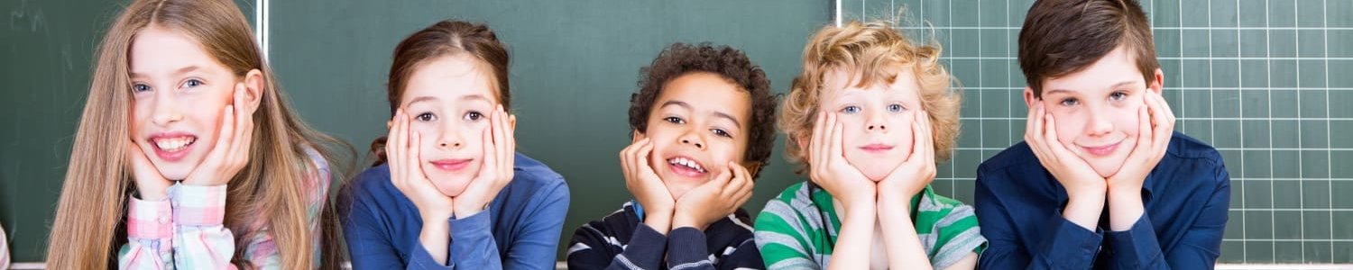 Schüler und Schülerinnen stützen sich vor einer Tafel mit ihren Ellenbogen auf Bücher und grinsen 