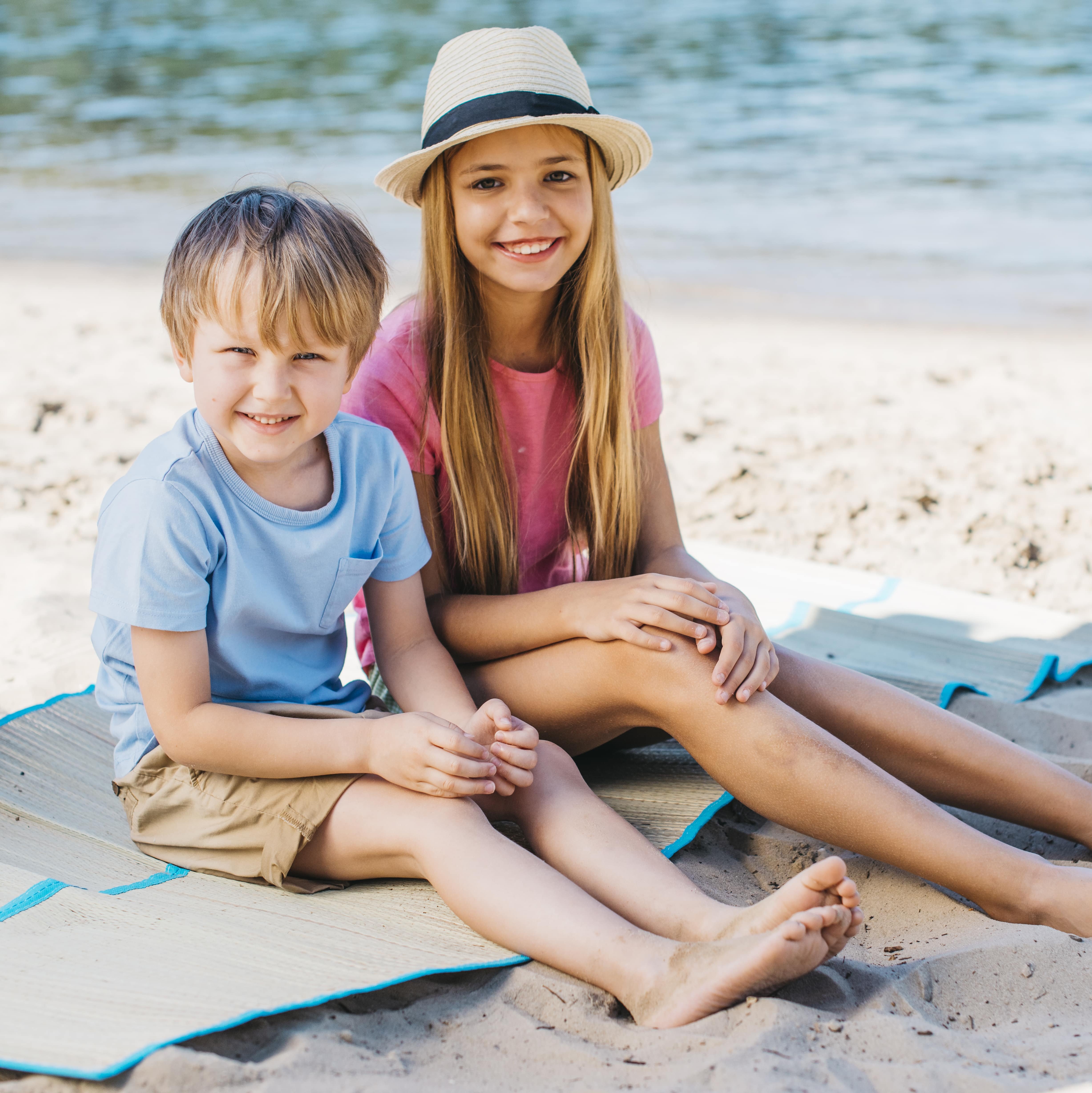 Kinder sitzen am Strand mit sommerliche Klamotten