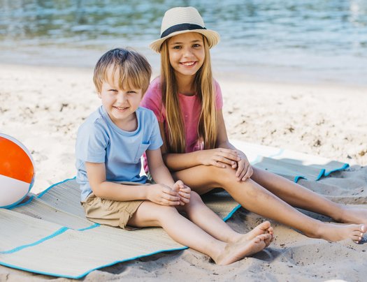 Kinder sitzen am Strand in sommerlichen Klamotten