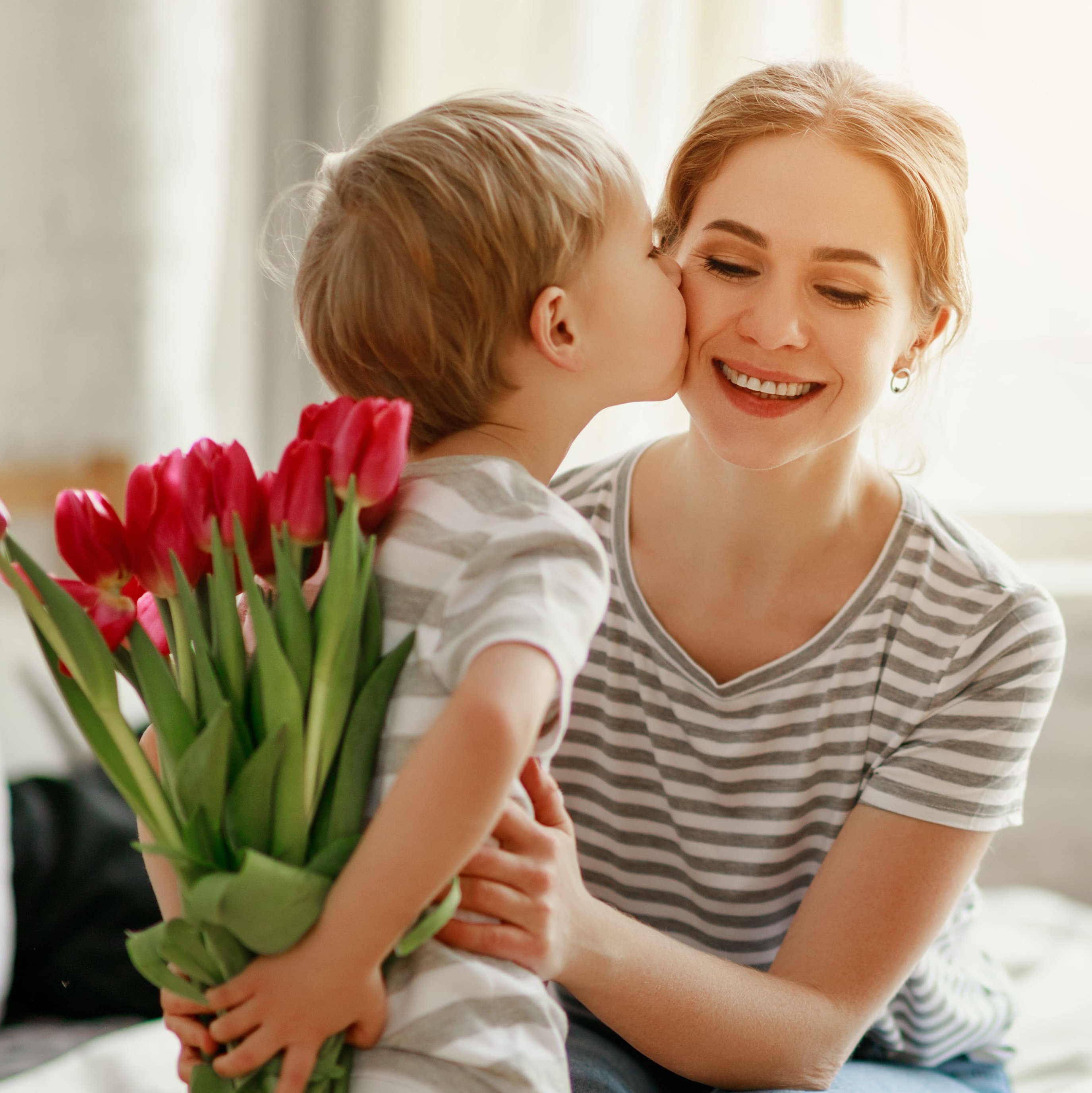 Junge hält Tulpen hinter seinem Rücken und küsst seine Mutter