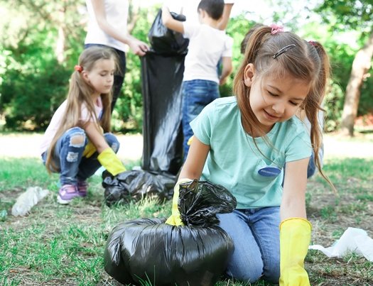 Schülerinnen und Schüler sammeln auf einer Wiese Müll.