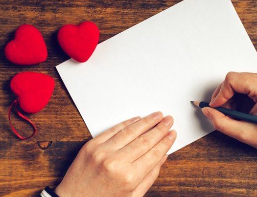 Jemand schreibt einen Liebesbrief; Briefpapier und rote Herzen liegen auf einem Tisch
