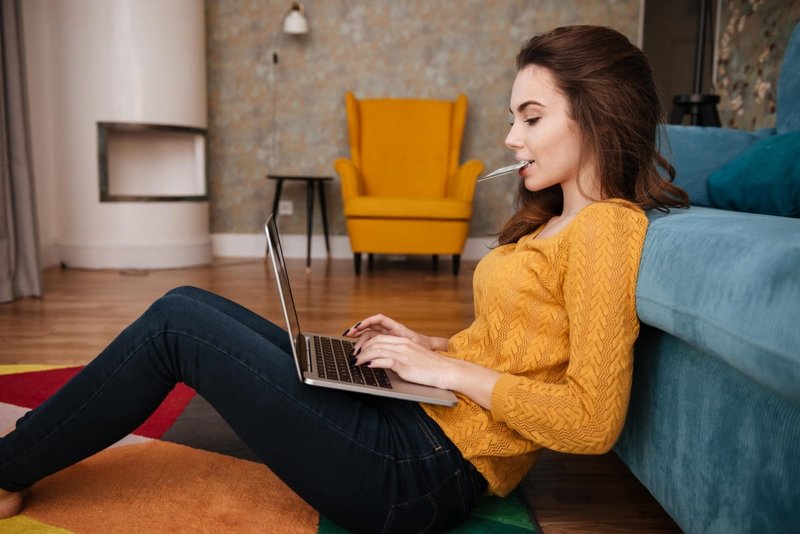 Frau sitzt am Laptop und hat EC-Karte im Mund