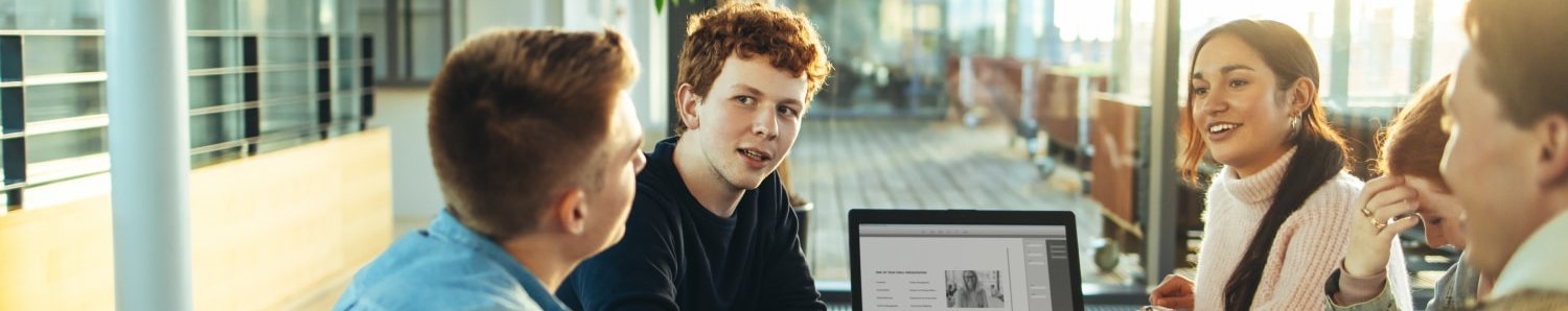 Dossier zu Unternehmerisches Denken und Handeln fördern Jugendliche diskutieren an rundem Tisch, Laptop mit Pitch in der Tischmitte