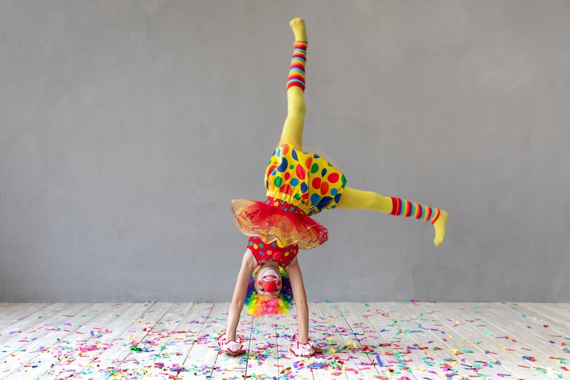 Ein Kind im Clownskostüm macht einen Handstand 