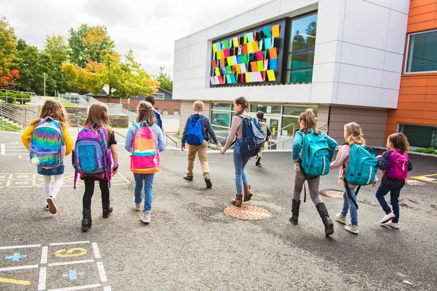 Schülerinnen und Schüler laufen auf ein Schulhaus zu