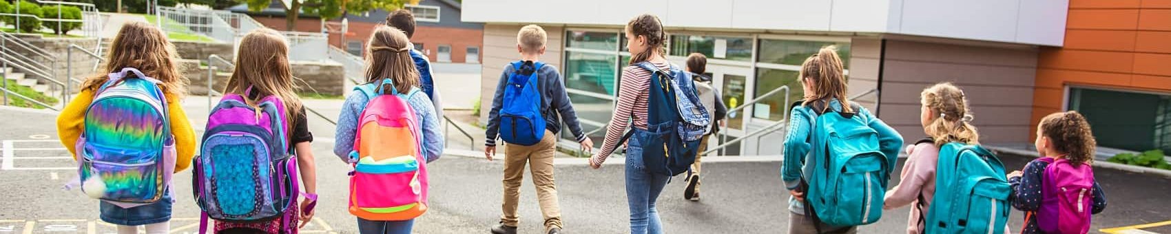 Schülerinnen und Schüler laufen auf ein Schulhaus zu 