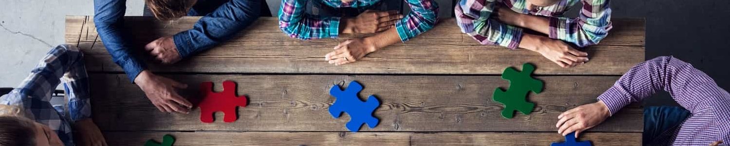 Puzzleteile auf einem Tisch, eine Gruppe sitzt um den Tisch und brainstormt