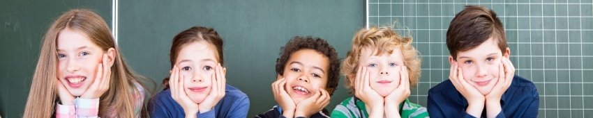 Schüler und Schülerinnen stützen sich vor einer Tafel mit ihren Ellenbogen auf Bücher und grinsen 