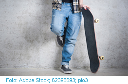 Junge lehnt an Wand mit Skateboard