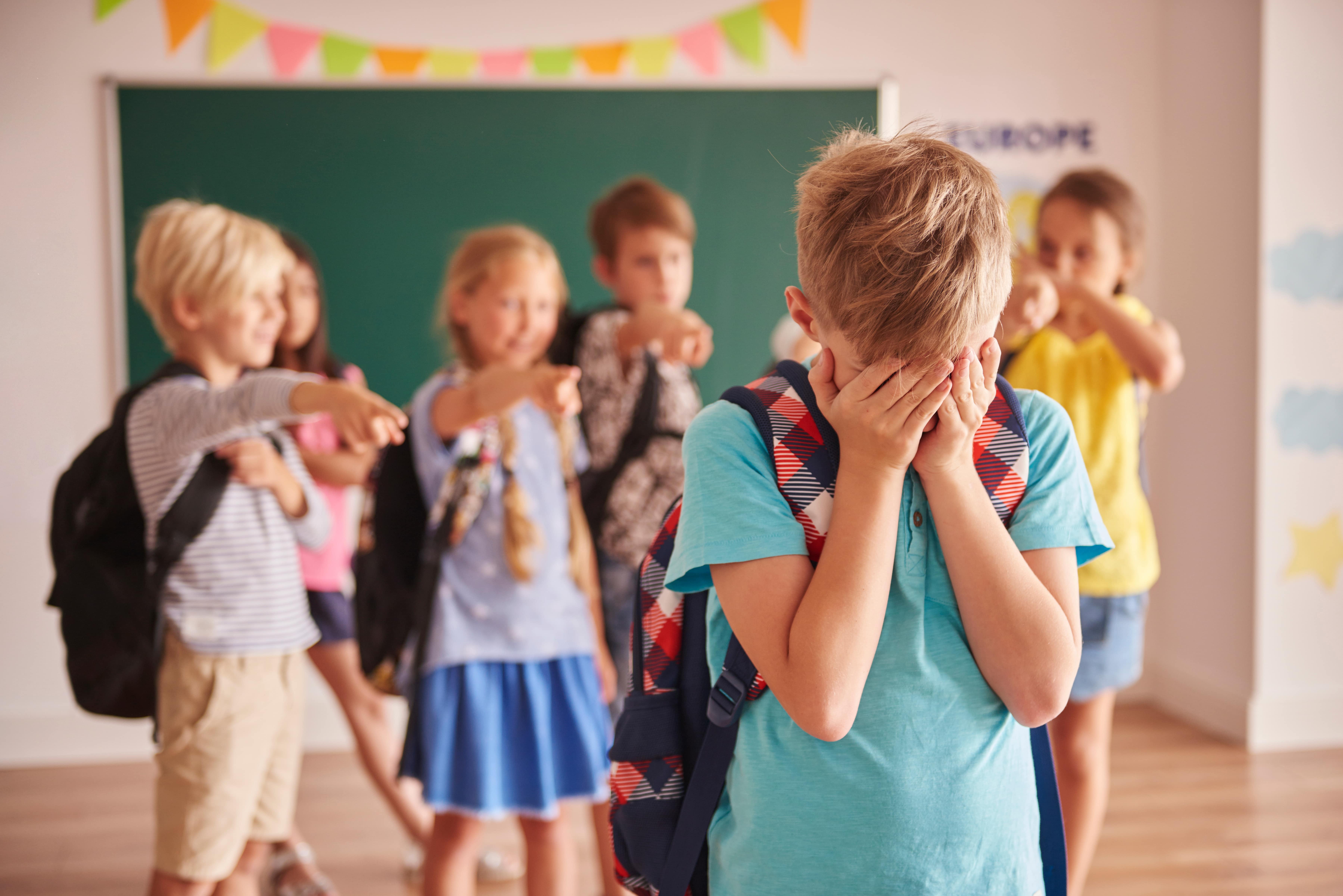 Schülerinnen und Schüler hänseln einen Mitschüler, zeigen auf ihn; der Junge weint