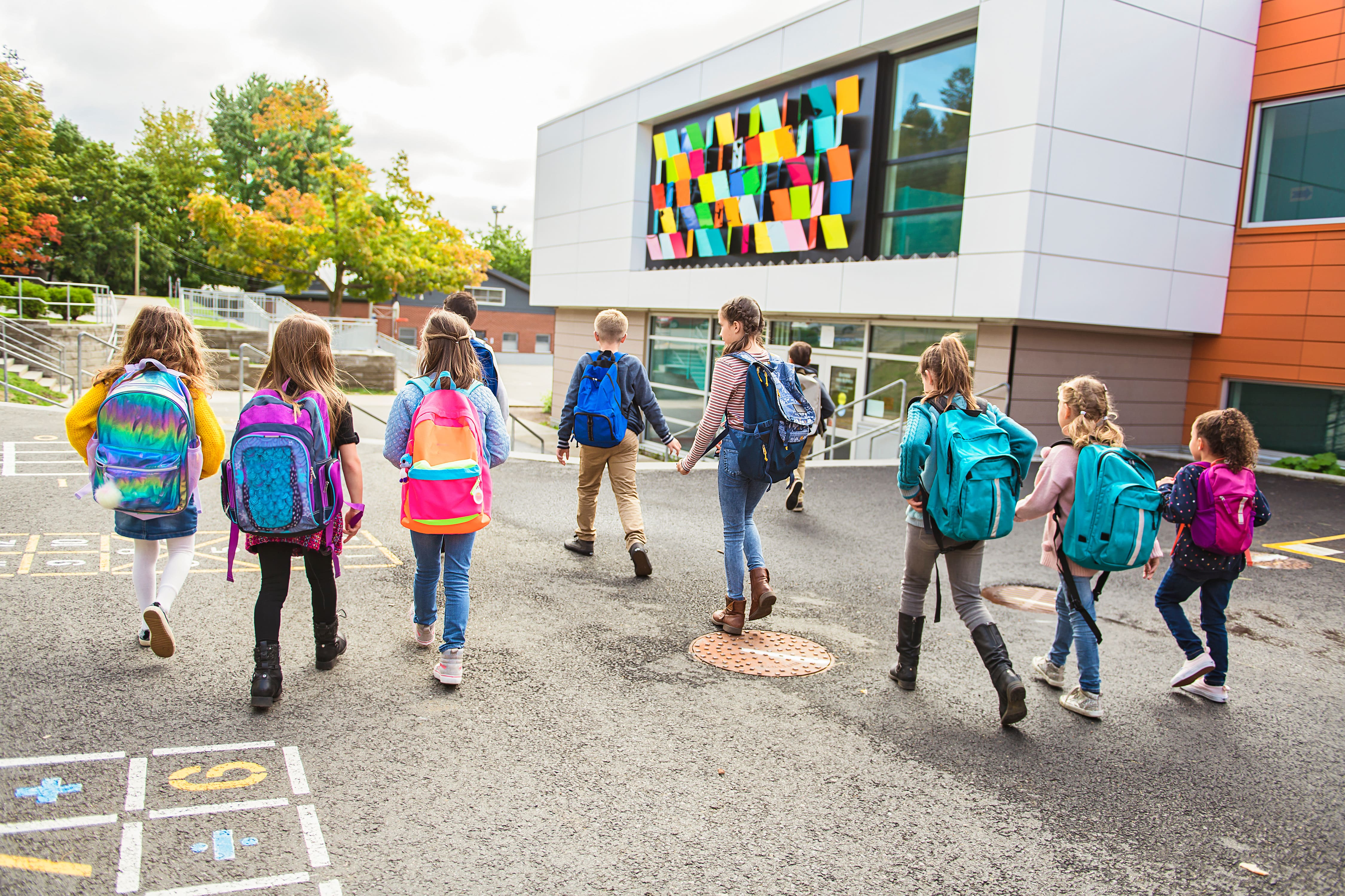 Schülerinnen und Schüler laufen auf ein Schulhaus zu