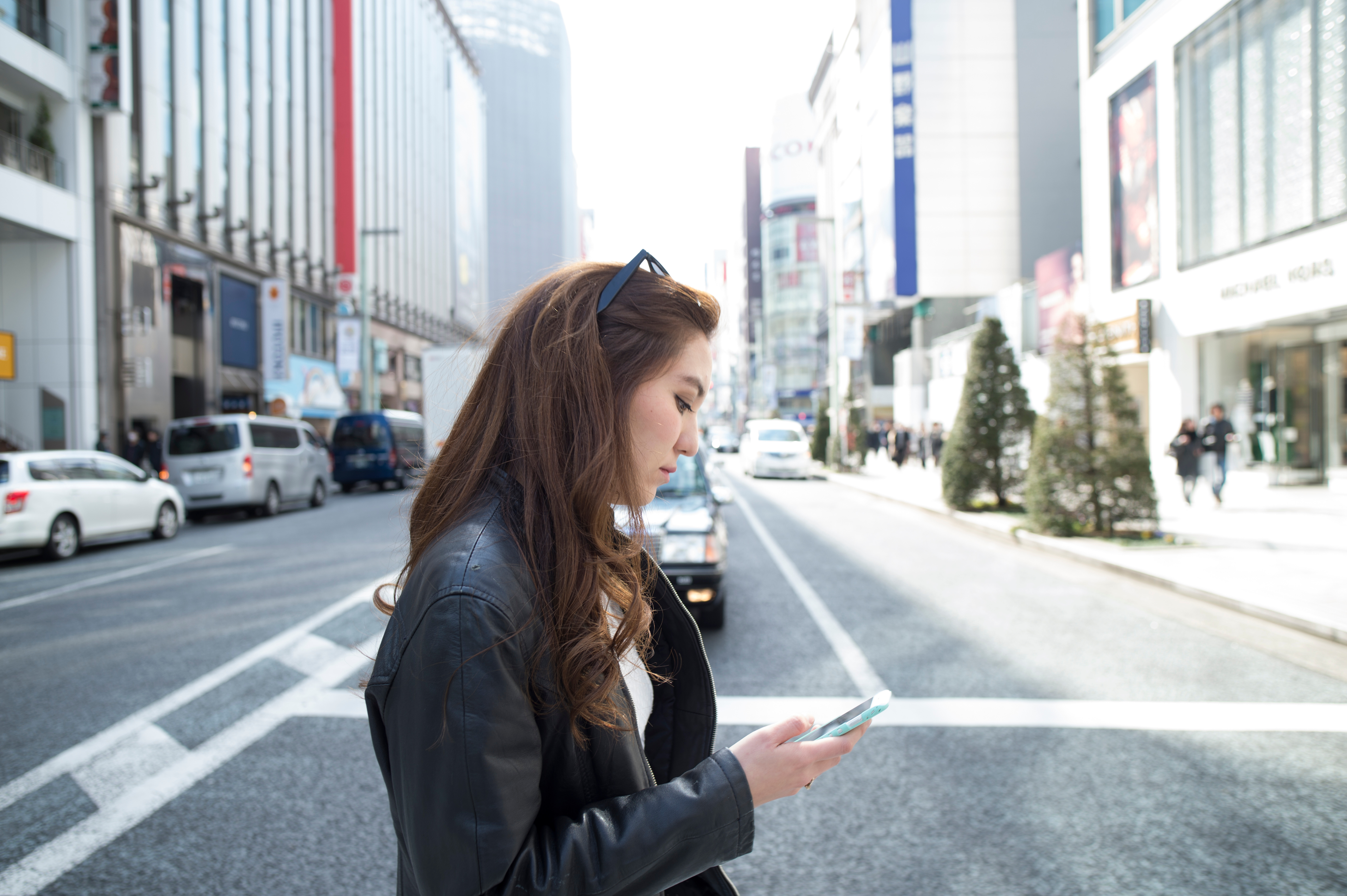 Junge Frau schaut während der Überquerung der Straße aufs Smartphone