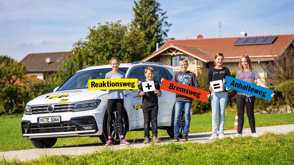 Kinder vor einem Auto; sie üben die Formel Reaktionsweg + Bremsweg = Anhalteweg