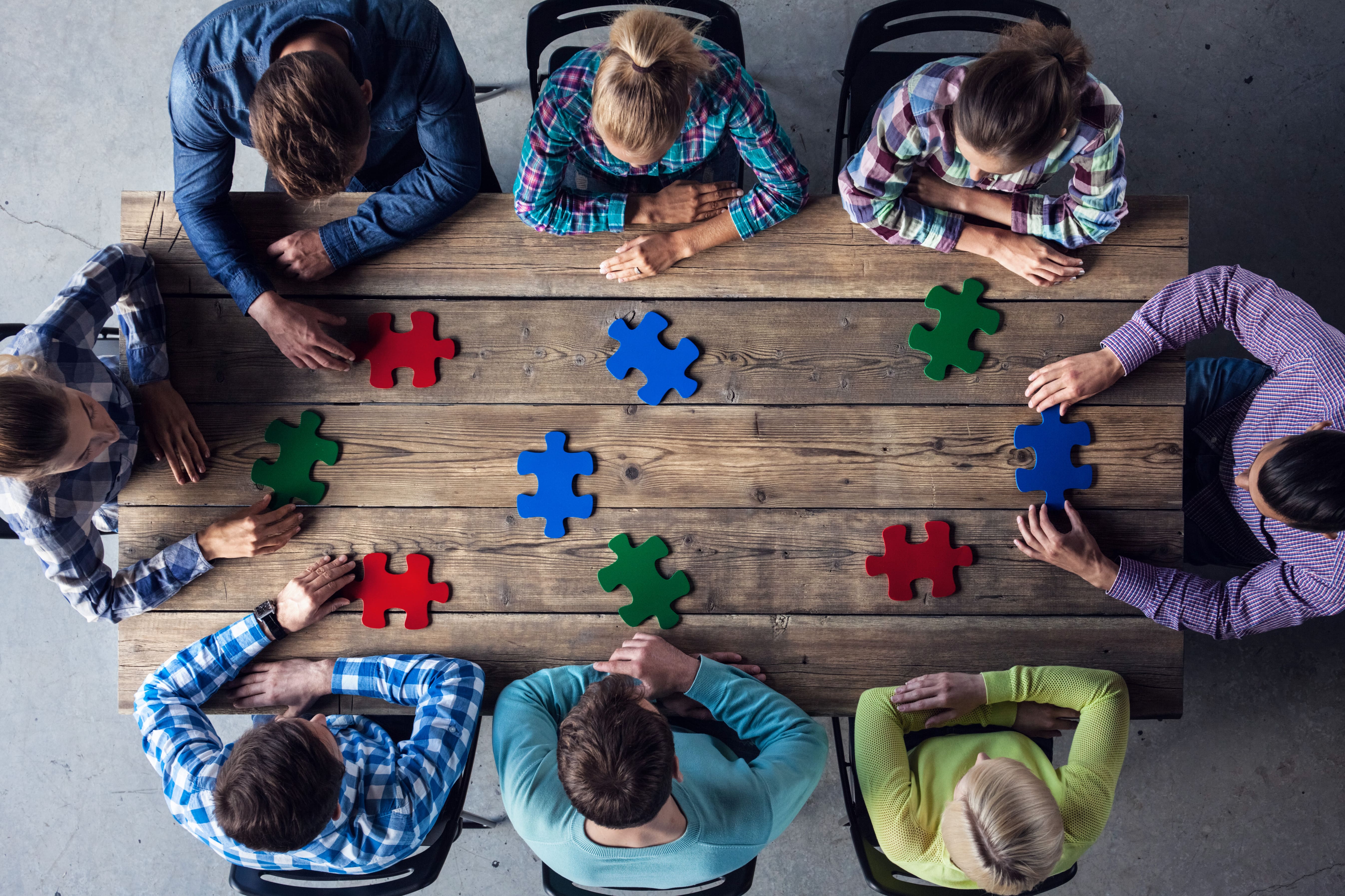 Puzzleteile auf einem Tisch, eine Gruppe sitzt um den Tisch und brainstormt