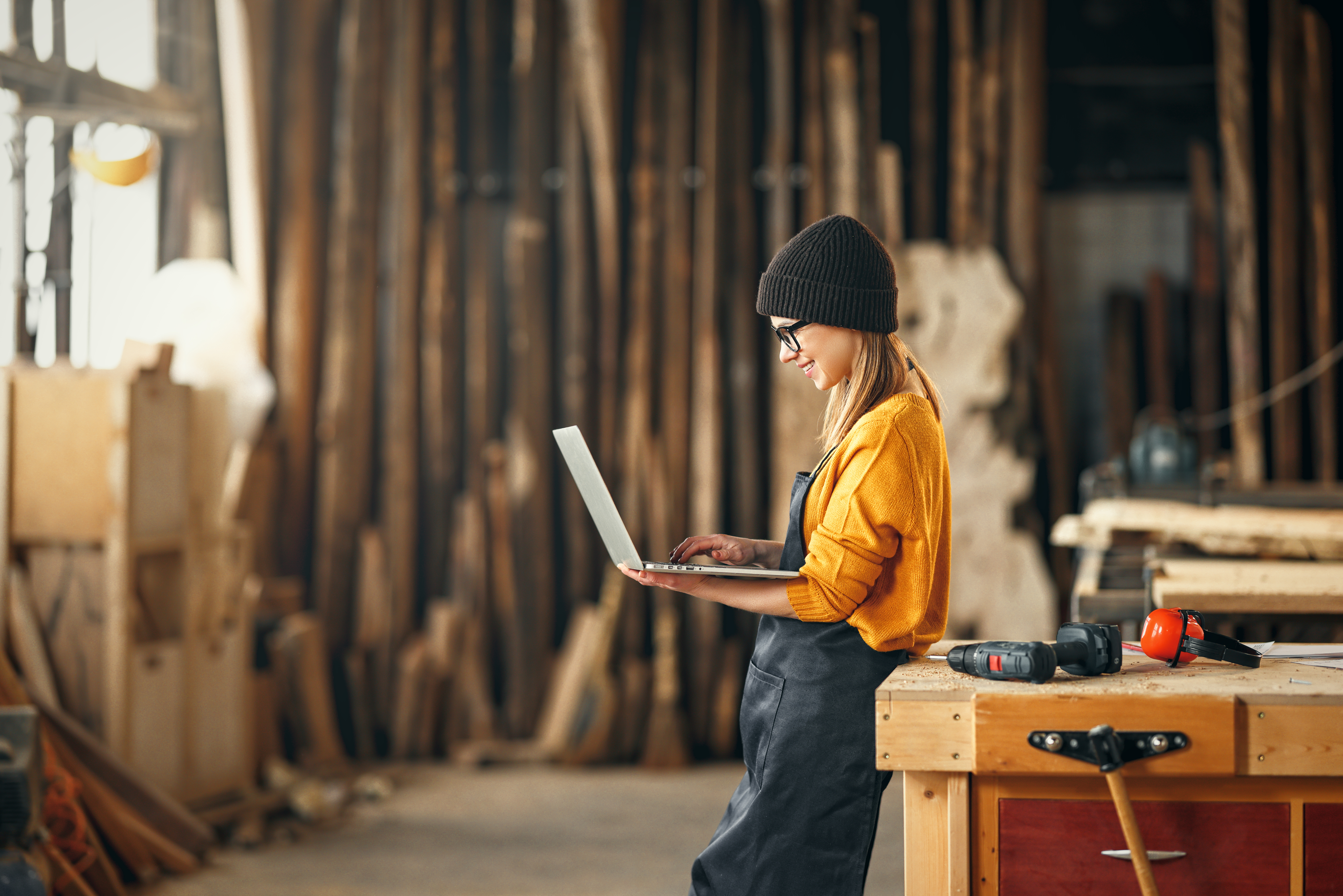 Junge Handwerkerin mit Laptop in Werkstatt