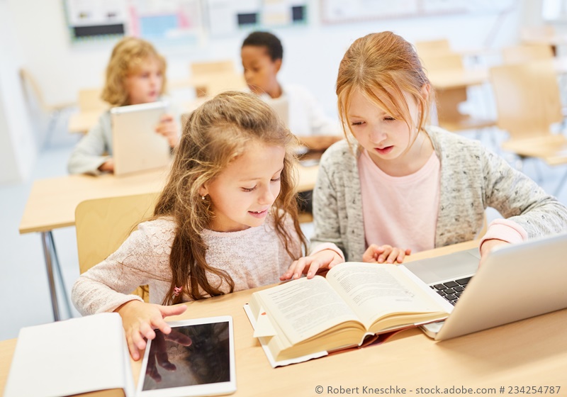 Mädchen arbeiten im Unterricht multimedial mit Laptop, Tablet und Buch