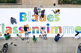 Kinder bemalen ein großes Banner, am Boden liegend, mit der Aufschrift "Blaues Klassenzimmer"