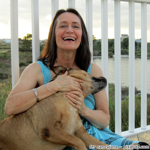 Frau lachend mit einem Hund auf und einem hohen weißen Geländer hinter sich
