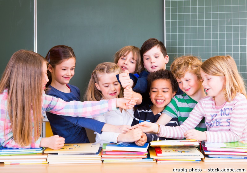 Kinder halten die Hände über einem Schulpult zusammen