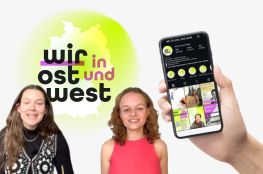 Zwei Mädchen vor dem Projektlogo von Wir in Ost und West, daneben eine Hand mit Handy